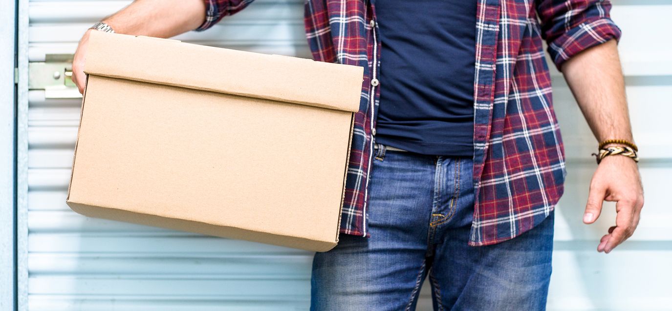 Oberkörper eines Mannes in kariertem Hemd, der eine geschlossene Pappschachtel hält.